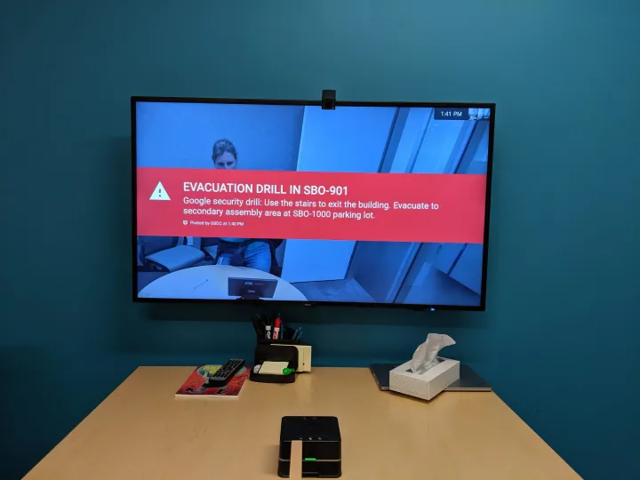 A Google Meet room display showing a red emergency alert banner across the screen.